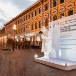 Белая фигура пожилой женщины со смартфоном у стенда на Арбате