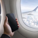 Пассажир держит смартфон у иллюминатора самолета